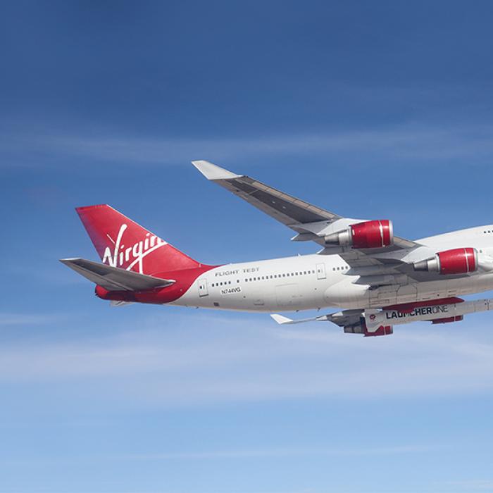 Virgin Orbit’s specially equipped Boeing 747 flies in blue skies with small rocket attached underneath