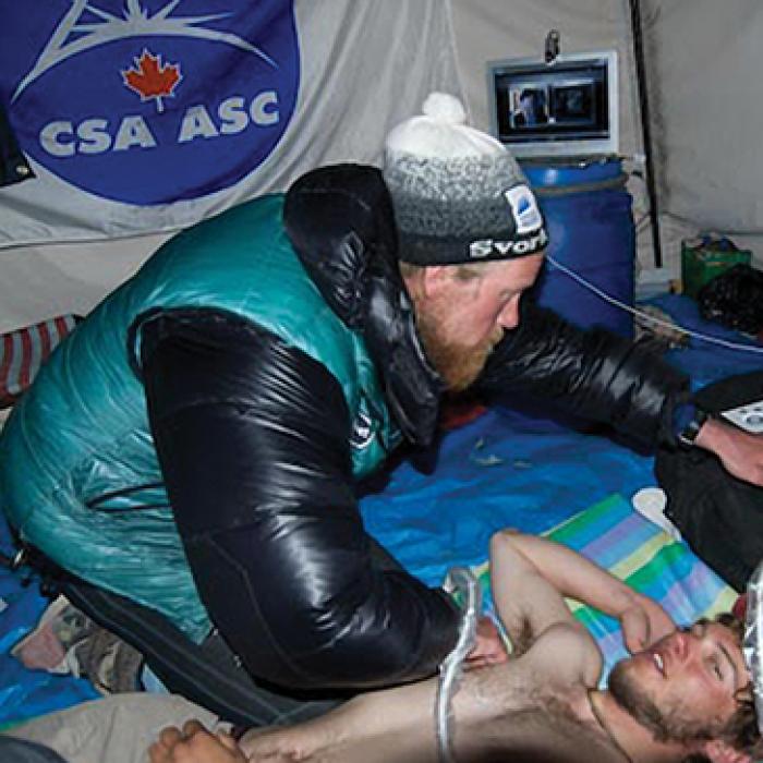 A mountain climber examines a colleague with ultrasound equipment.