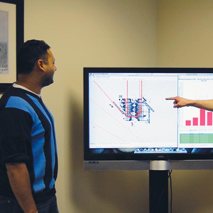 Two analysts view ground traffic patterns on a large monitor