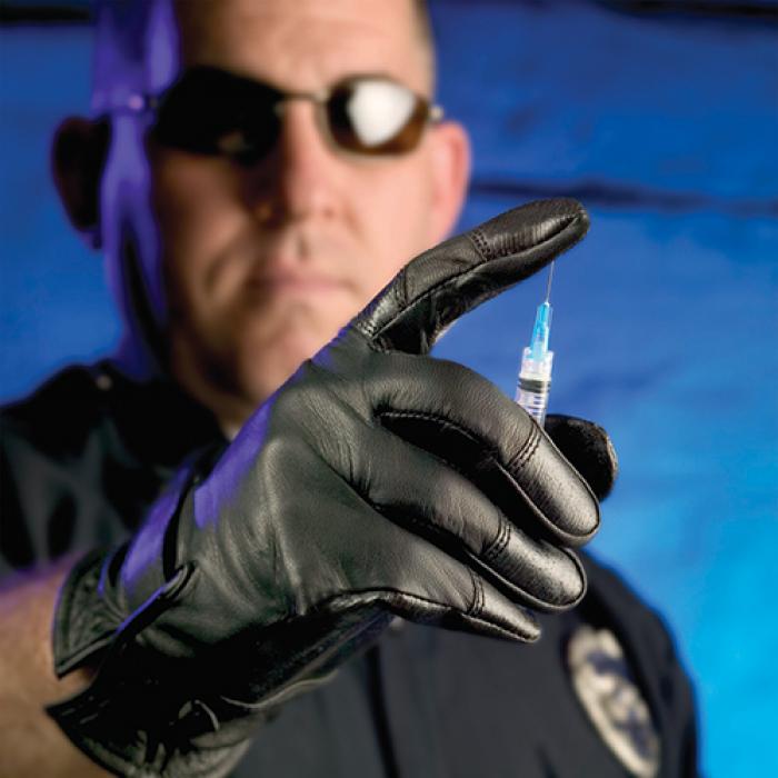 Available in the TurtleSkin line are puncture-resistant and needle-resistant clothing, such as these gloves. The TurtleSkin products are in use by various law enforcement groups around the world. A police officer presses a Turtleskin-gloved finger onto a needle