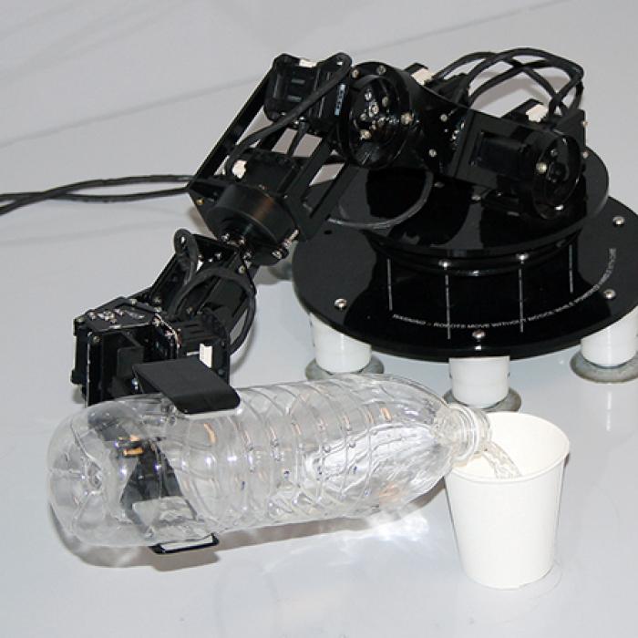 A small robot claw pouring water from a bottle into a cup