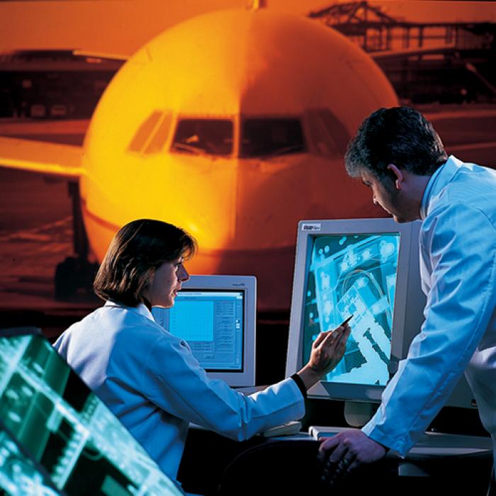 A man and a woman view radiography on computers with an image of a plane behind them