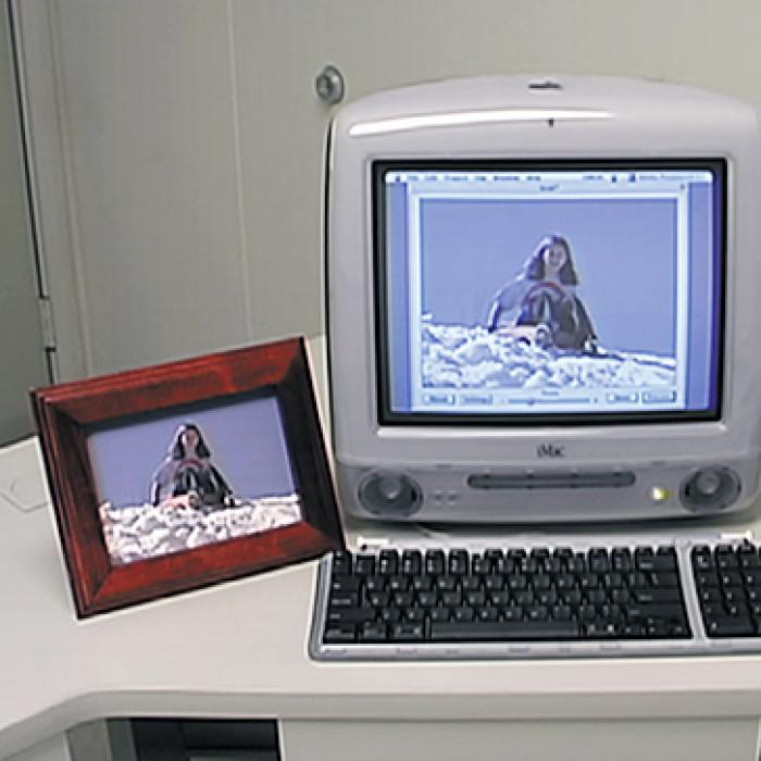An imac with an image on the screen, a framed image and a video camera beside it.
