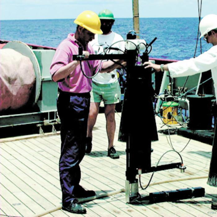 SeaSpec spectroradiometer on the deck of a ship with two men holding onto it and another man standing in background