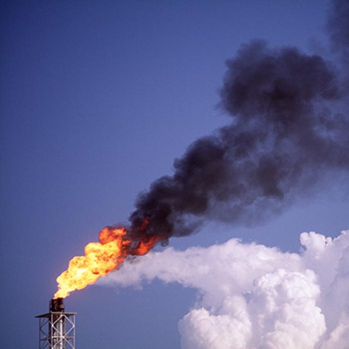 Flare stack with white cloud in background at oil refinery