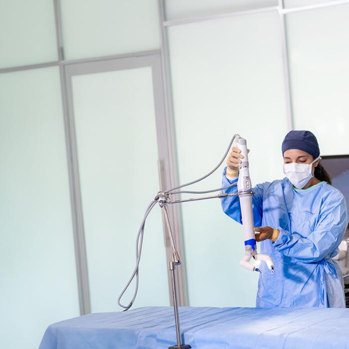 Man in scrubs sitting at a computer behind a woman in scrubs positioning device over operating table