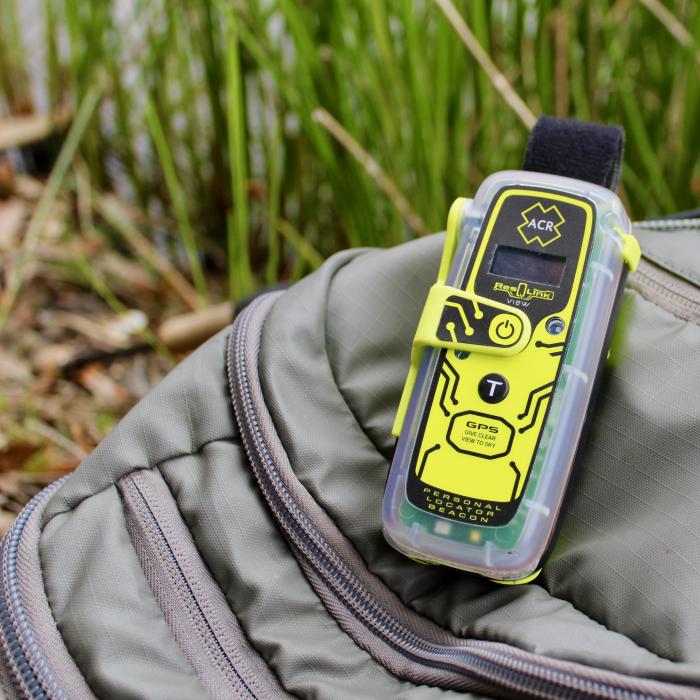 A neon yellow and black ResQLink device laying on a beige bag in an outdoor setting with tall grasses blurred in the background.
