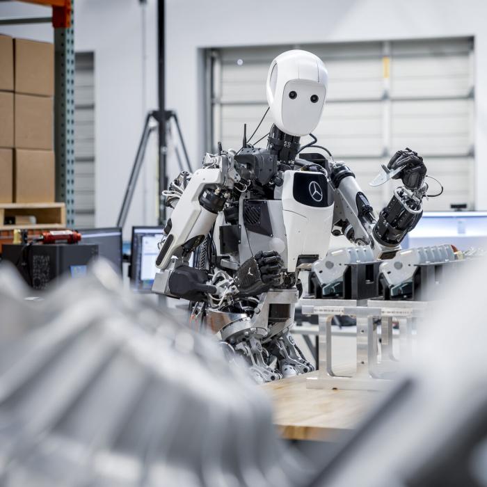 A white and black, humanoid robot holds a blade or machine part in a factory setting. 