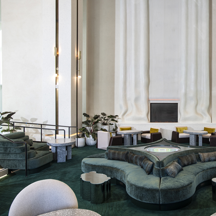 High-ceilinged lounge area with curvy green couches and a wall in the shape of bunched curtains. 