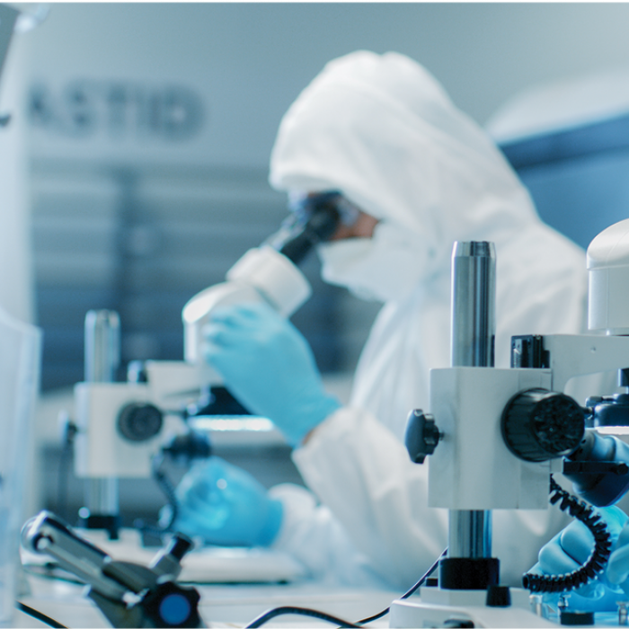 Workers in clean-room suits look through microscopes