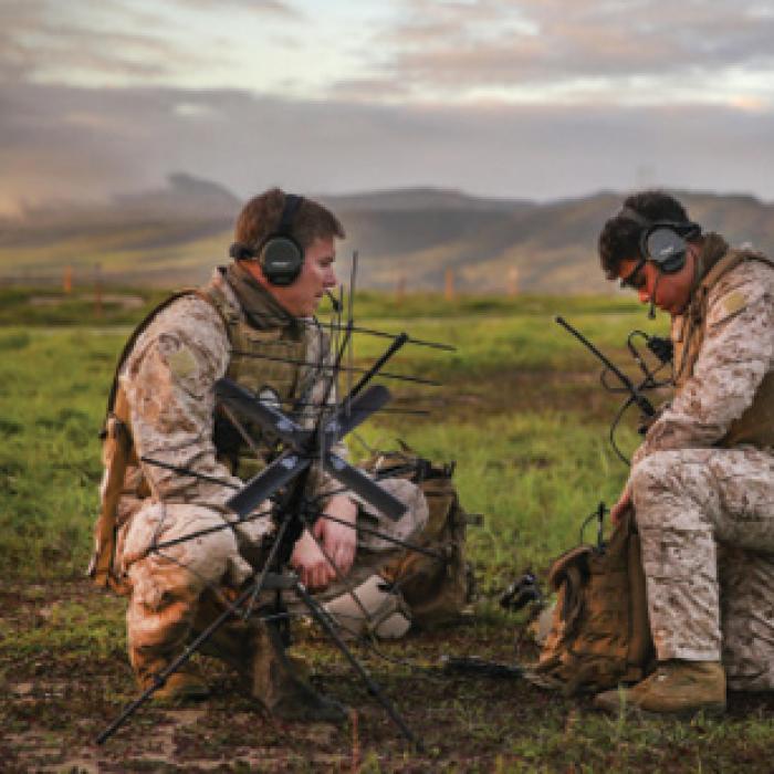 Two male servicemembers set up communications equipment in the field