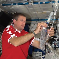 An astronaut on the space station works with the prototype water purification system based on membranes infused with aquaporins