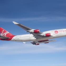 Virgin Orbit’s specially equipped Boeing 747 flies in blue skies with small rocket attached underneath