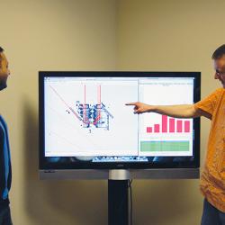 Two analysts view ground traffic patterns on a large monitor