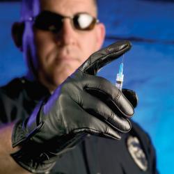 Available in the TurtleSkin line are puncture-resistant and needle-resistant clothing, such as these gloves. The TurtleSkin products are in use by various law enforcement groups around the world. A police officer presses a Turtleskin-gloved finger onto a needle