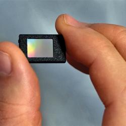 A thumb and forefinger hold a thumbnail-sized microdisplay panel.