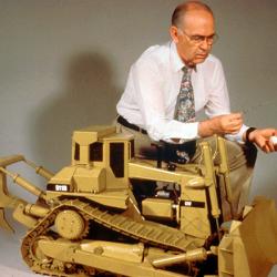 A researcher kneels down next to a 1/8 scale replica of the world’s largest earthmover caterpillar tractor