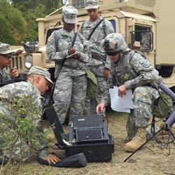 Service members in camouflage dress crowd around field communication equipment