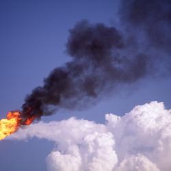 Flare stack with white cloud in background at oil refinery
