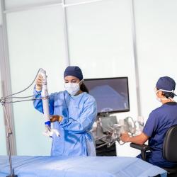 Man in scrubs sitting at a computer behind a woman in scrubs positioning device over operating table