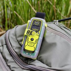 A neon yellow and black ResQLink device laying on a beige bag in an outdoor setting with tall grasses blurred in the background.
