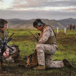 Two male servicemembers set up communications equipment in the field